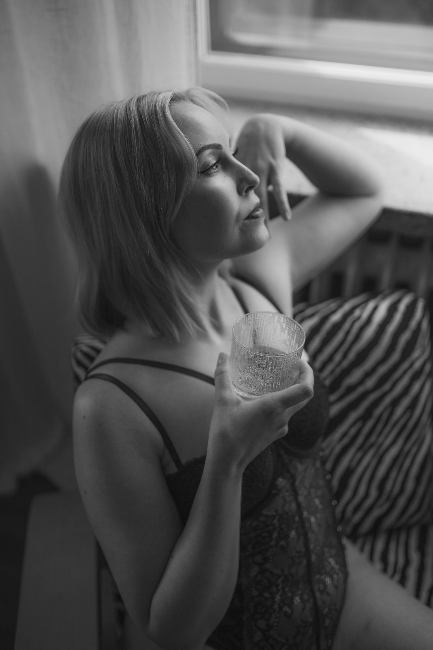 Naisen mustavalkoinen boudoir -muotokuva pehmeässä ikkunavalossa