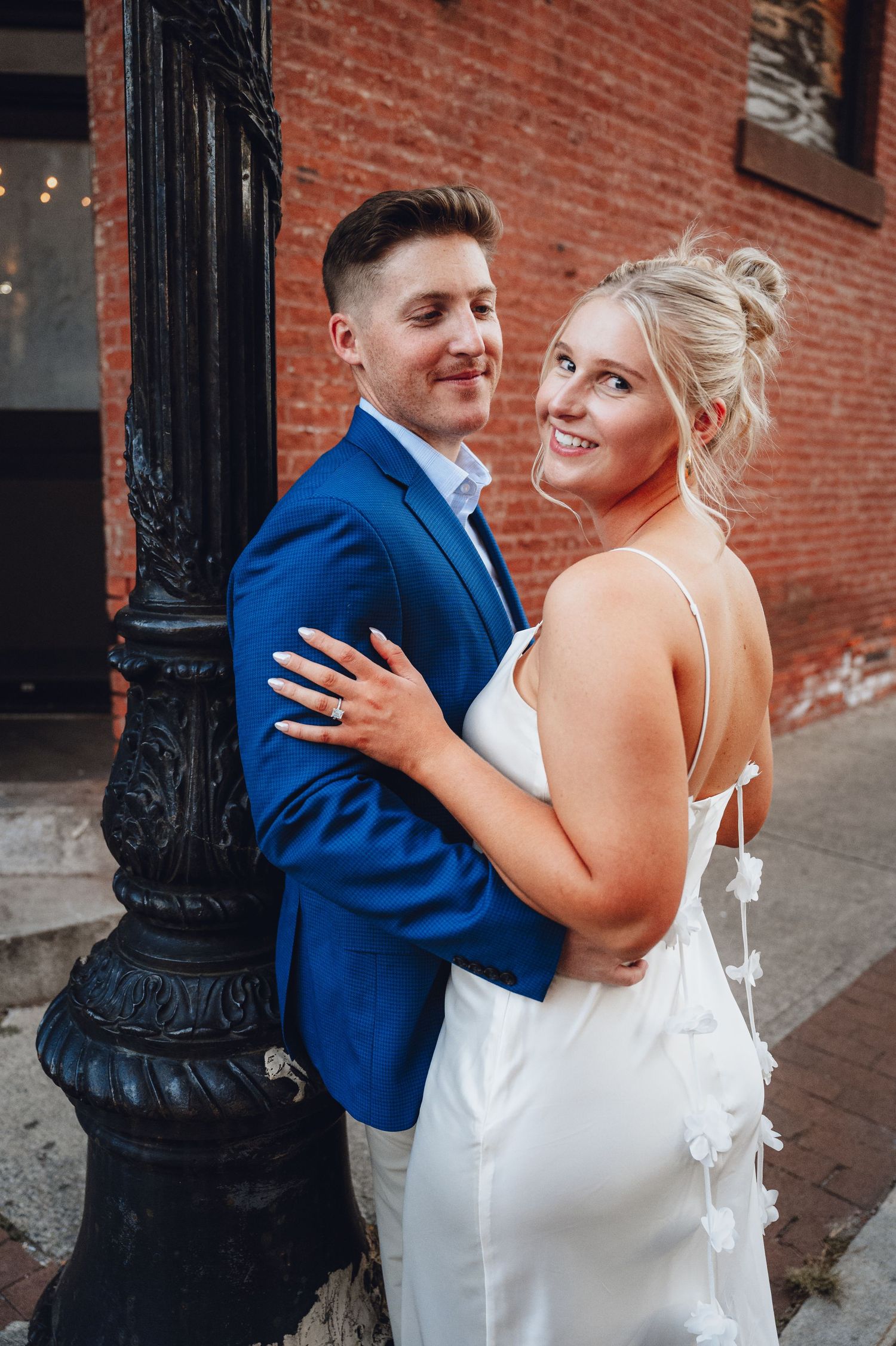 A couple shares a joyful moment together against a brick wall background during their wedding photoshoot.