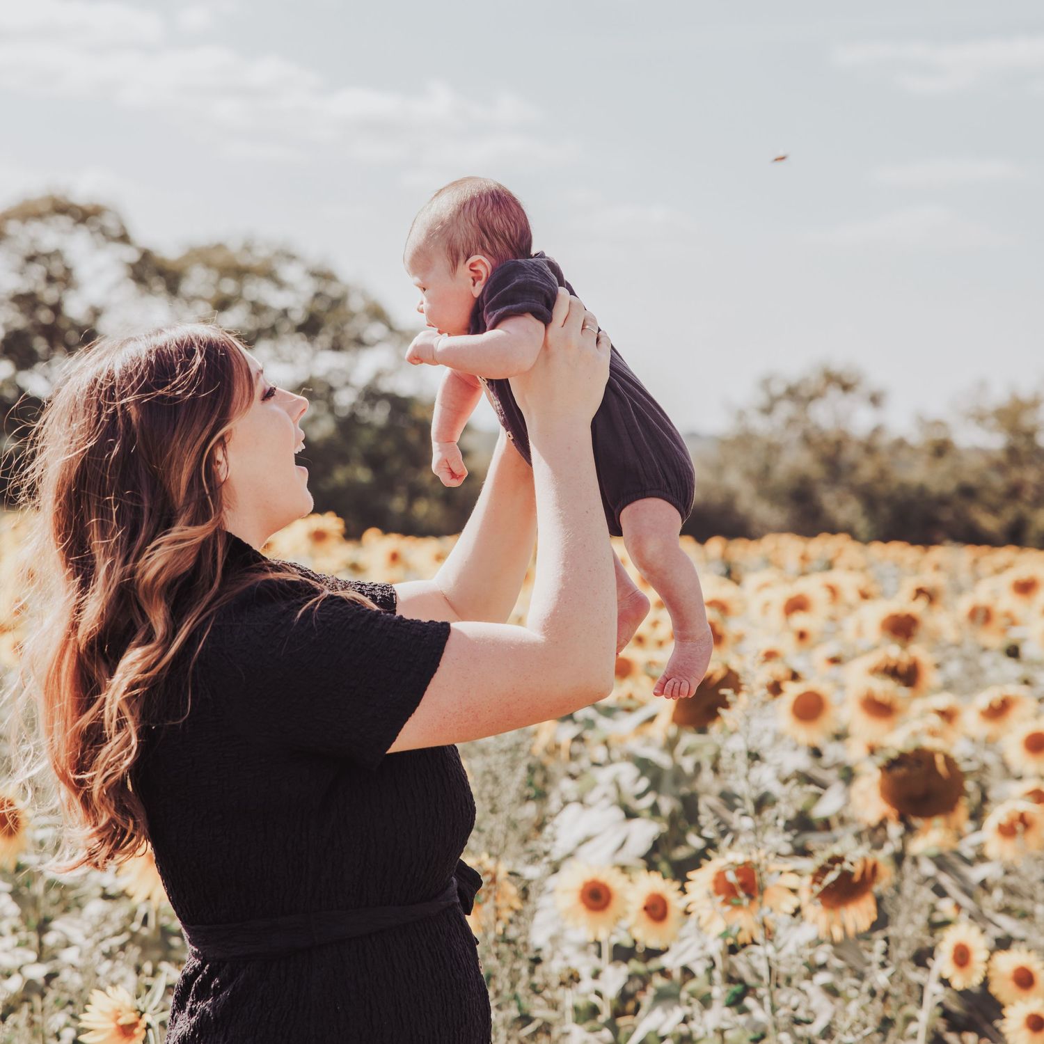 Mother lifting her newborn baby in a sunflower field during a natural outdoor photoshoot.