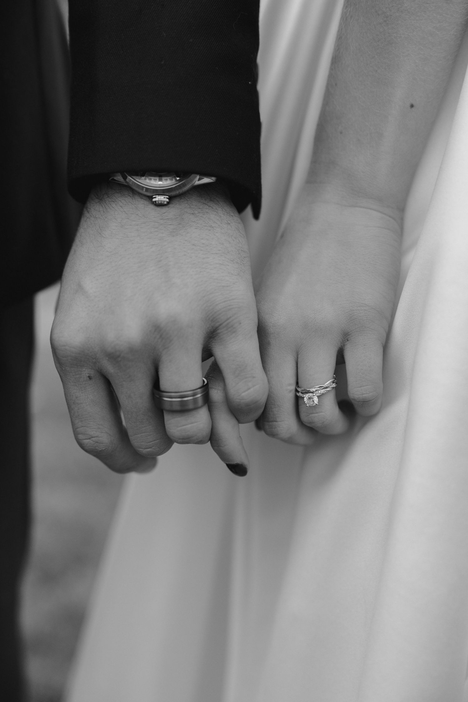Black and white close-up of hands showing wedding rings against a white background.