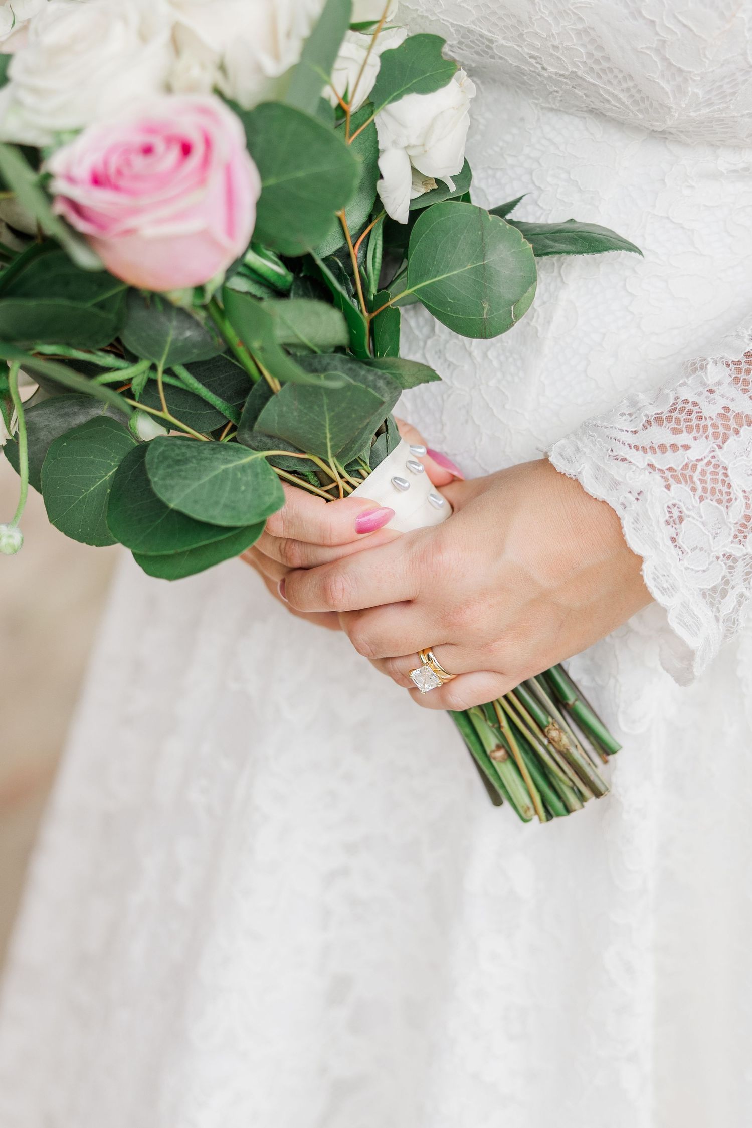 Close-up view of pink roses in a wedding bouquet held against white lace dress fabric.