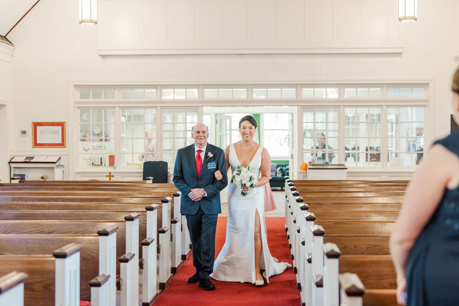 Interior view of a traditional church with wooden pews and white walls during a wedding ceremony.