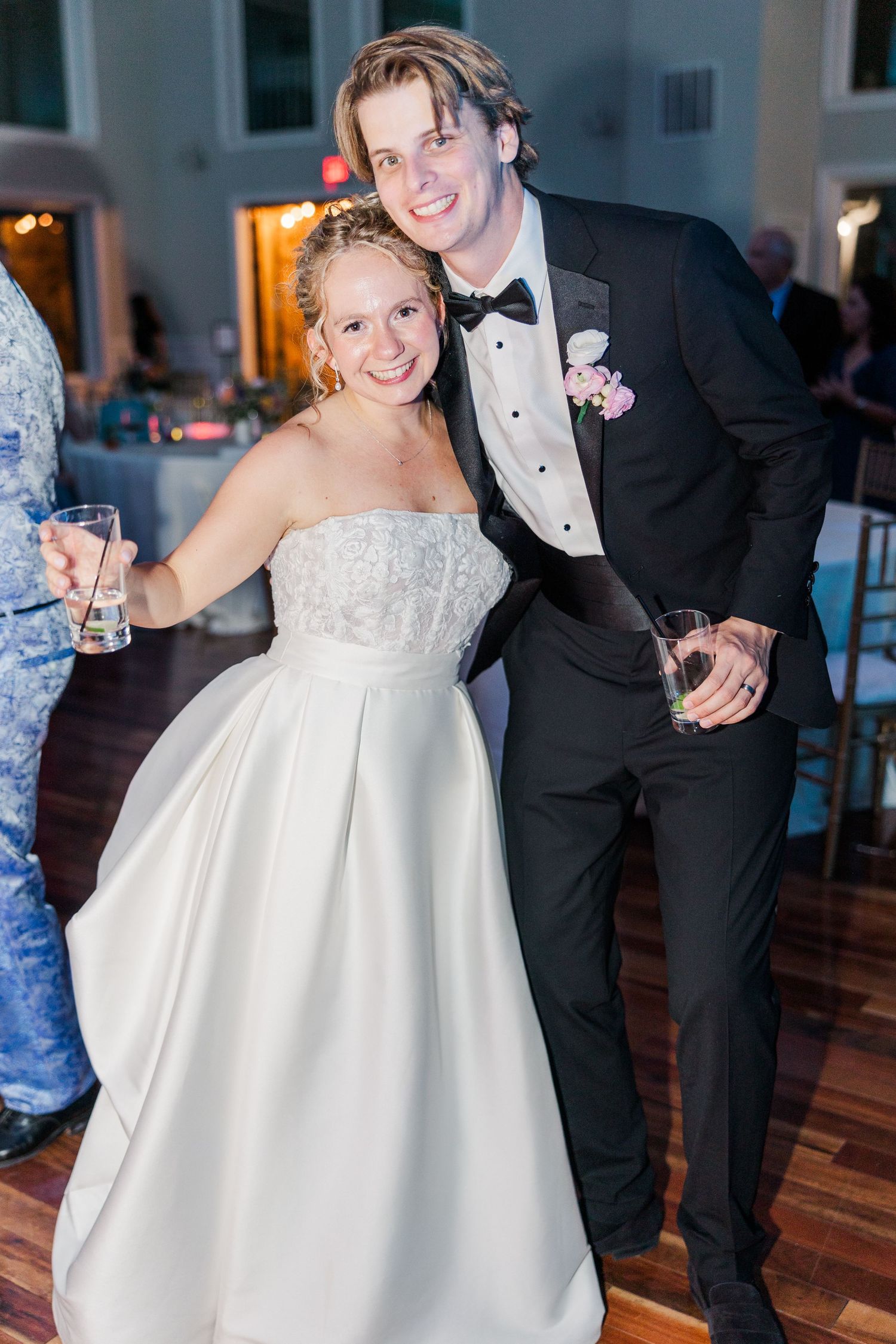 A couple celebrates at their wedding reception, with the bride in a white strapless gown and groom in classic tuxedo.