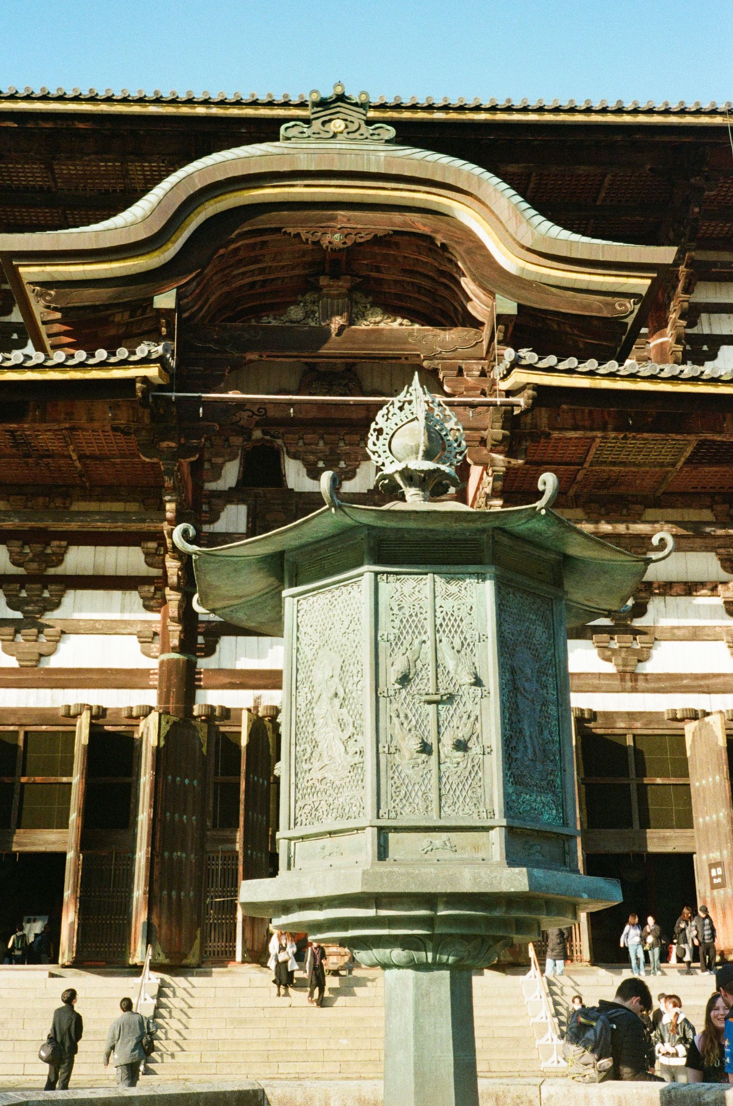Bronze lanterns with ornate traditional Japanese architecture line the pathway at a historic temple.