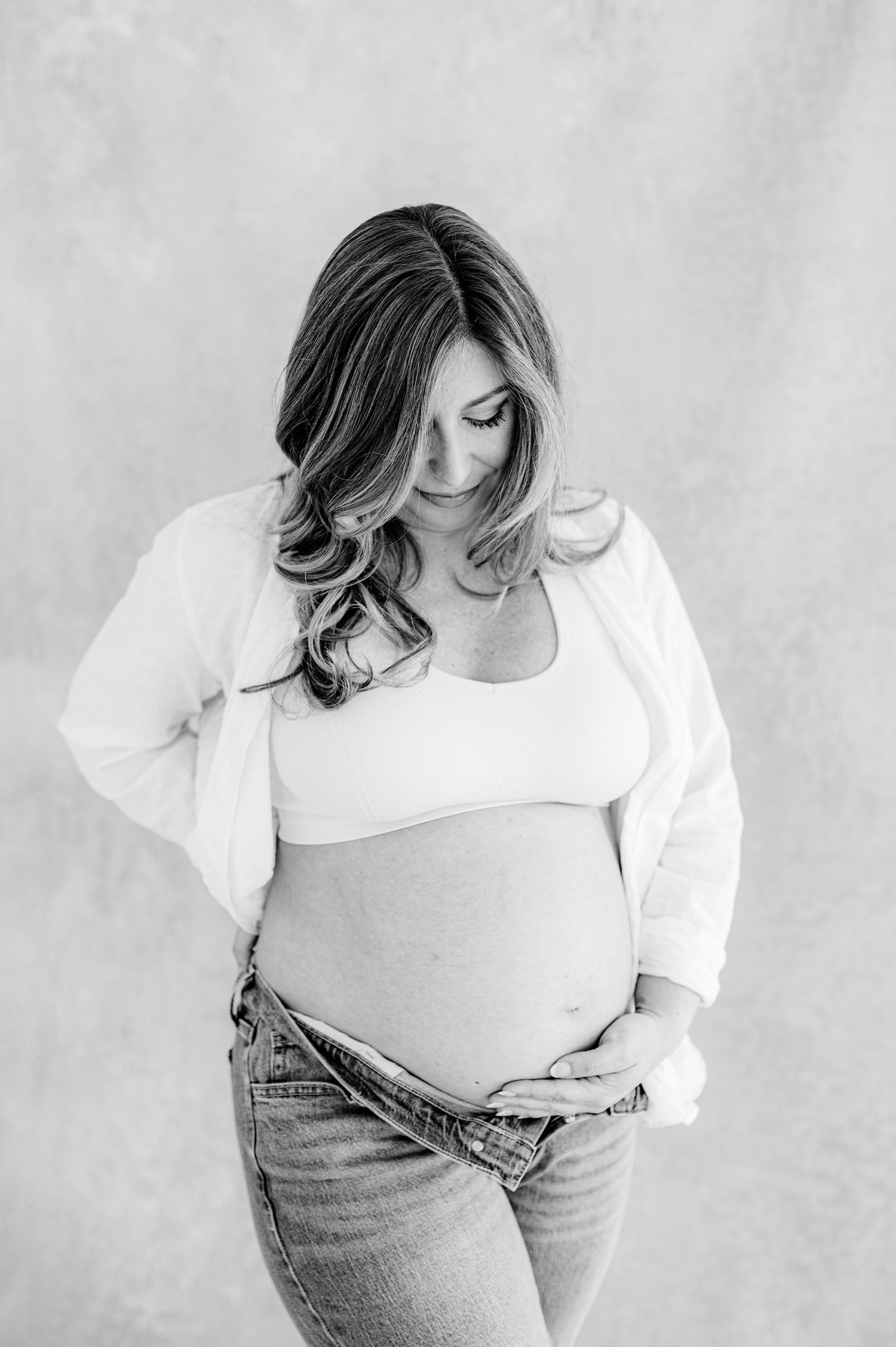 Maternity photo showing an expectant mother in jeans and white top looking down at her baby bump during maternity photoshoot in Jacksonville