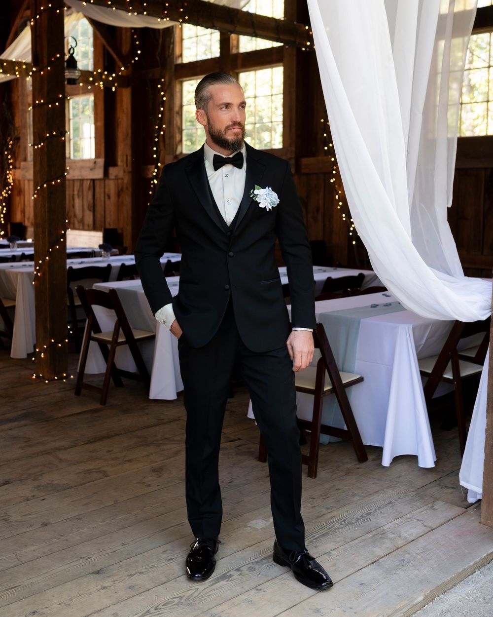 Wedding reception venue interior decorated with twinkling lights and white drapes in rustic barn setting.