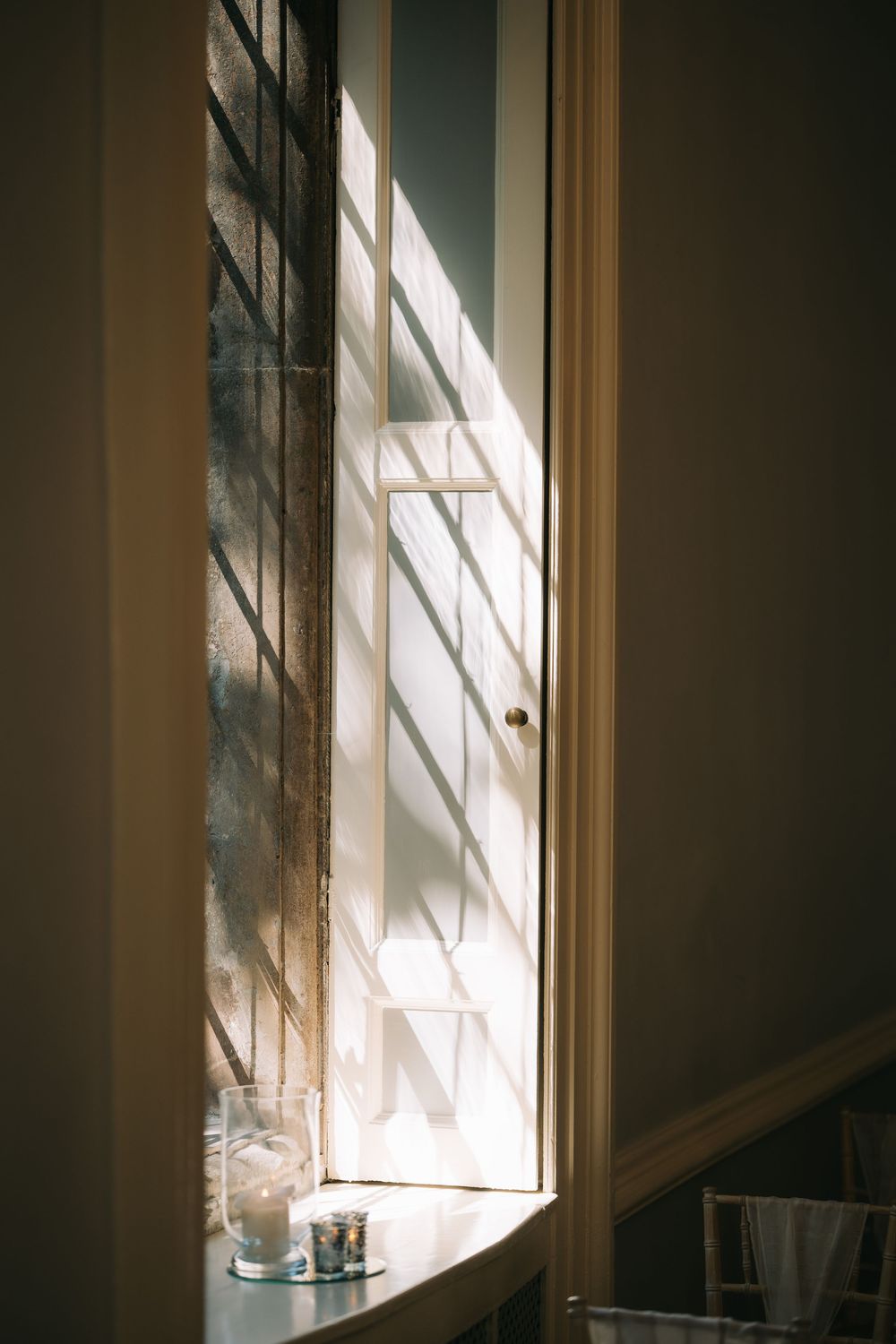 Sunlight streams through a window creating dramatic shadows on a white interior wall.