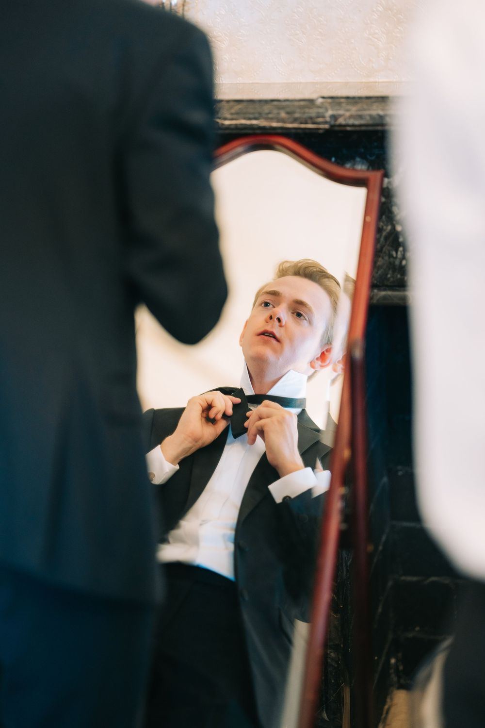 Getting ready moments captured in mirror reflection as formal attire is adjusted before the ceremony.