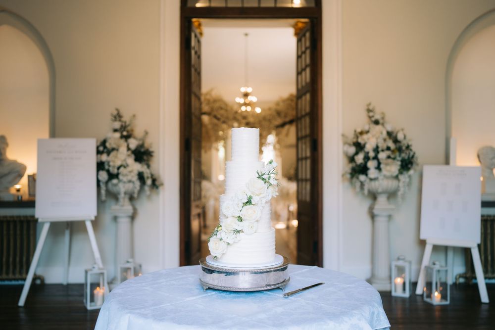 Elegant white wedding cake display in a bright, classic interior with greenery accents.