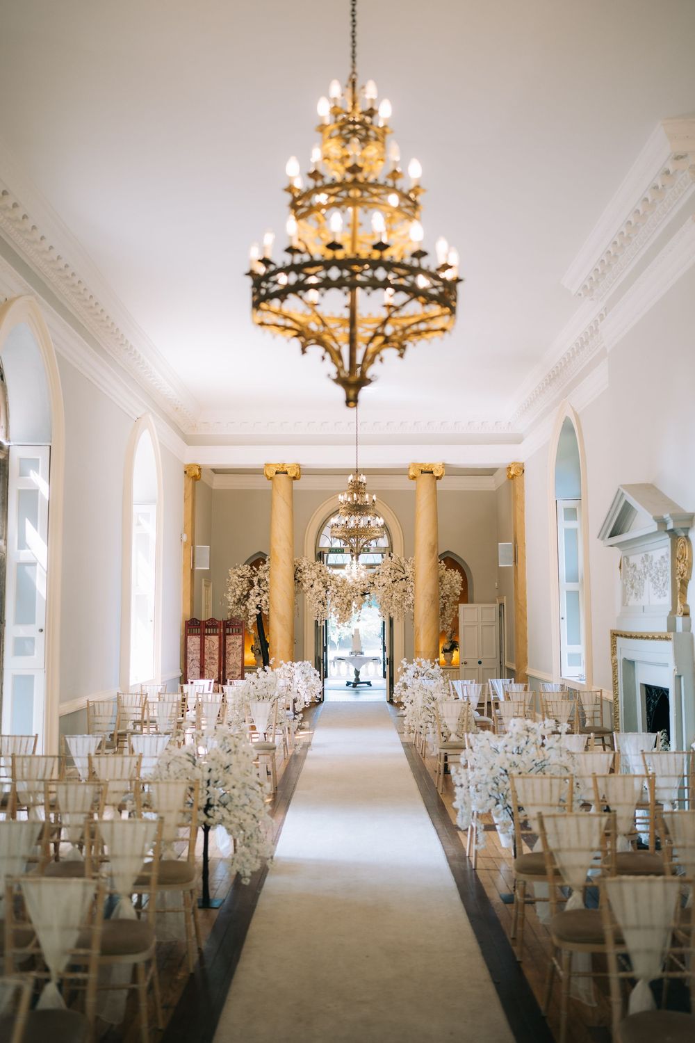 Elegant wedding ceremony venue with ornate chandelier and rows of white chairs along a center aisle.