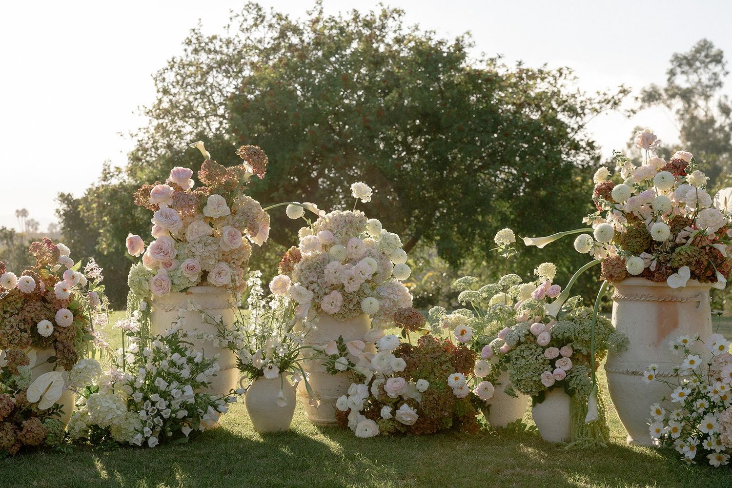 Elegant white floral arrangements in vases create a romantic garden display at sunset with soft golden lighting.