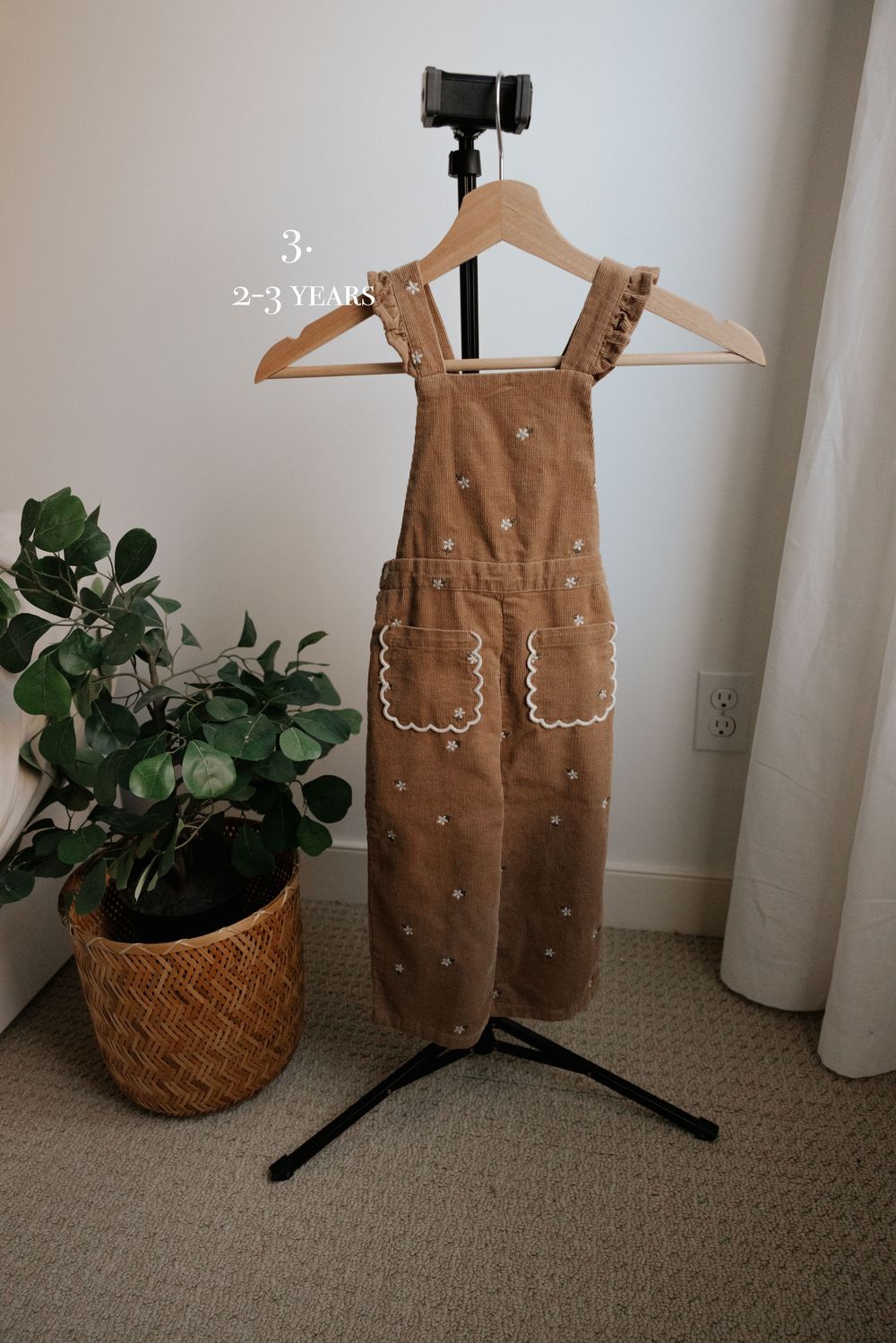 Brown corduroy overalls with white polka dots and scalloped pockets on display stand.