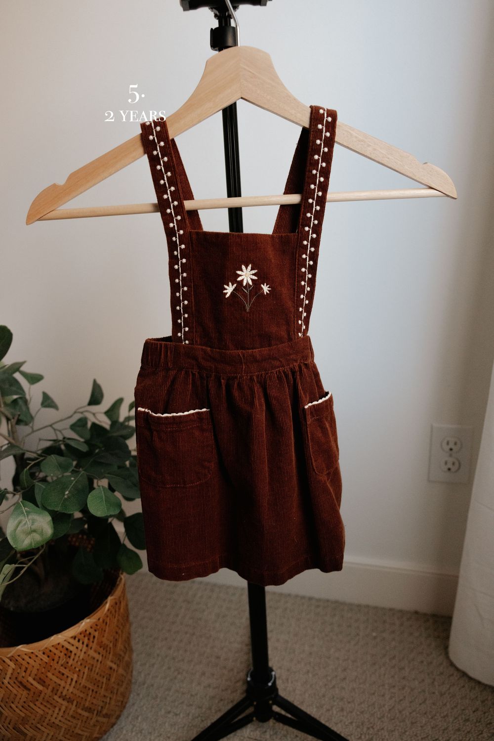 Brown velvet jumper dress with embroidered details displayed on wooden hanger.