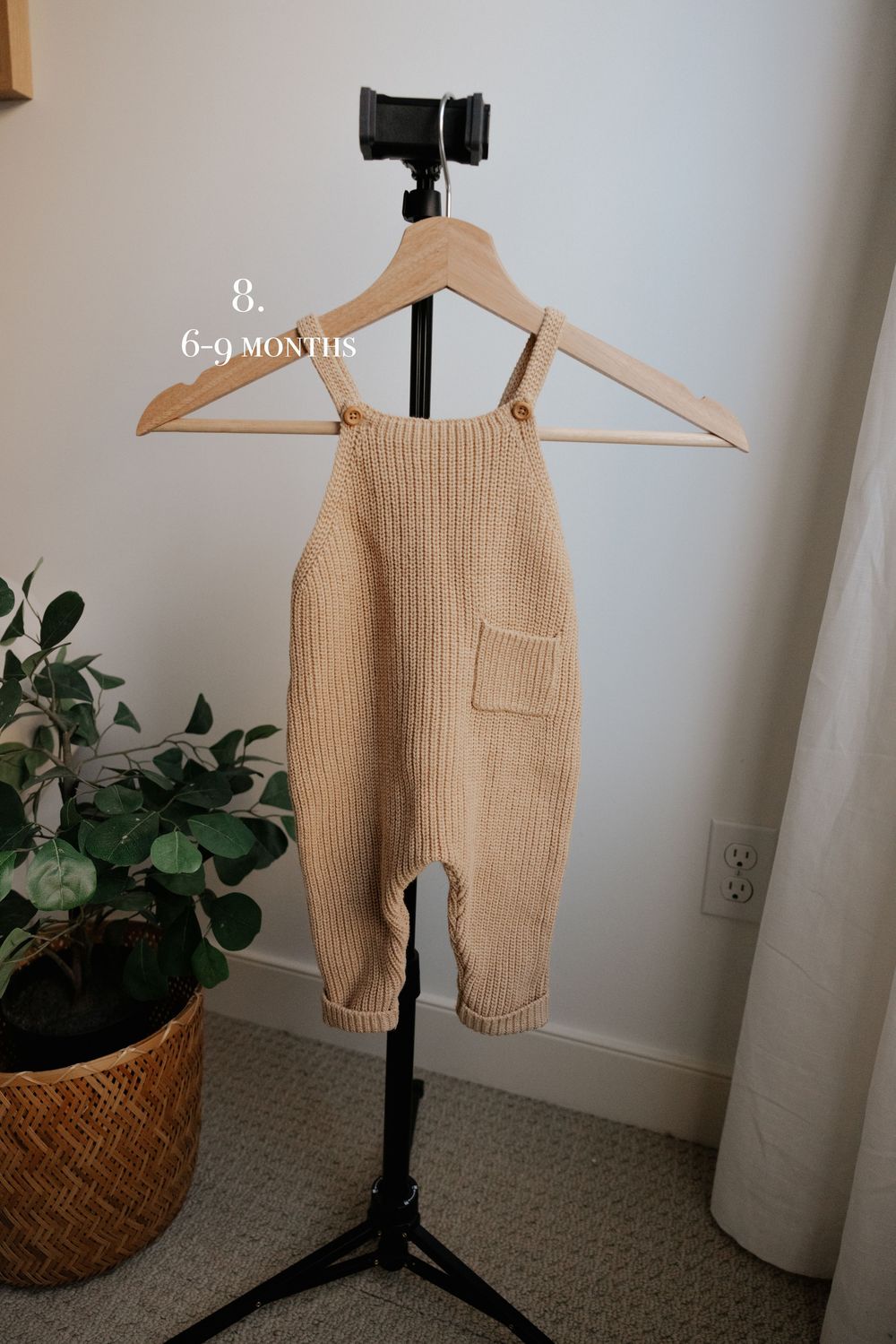 Beige ribbed knit baby pants with side pocket displayed on wooden hanger.