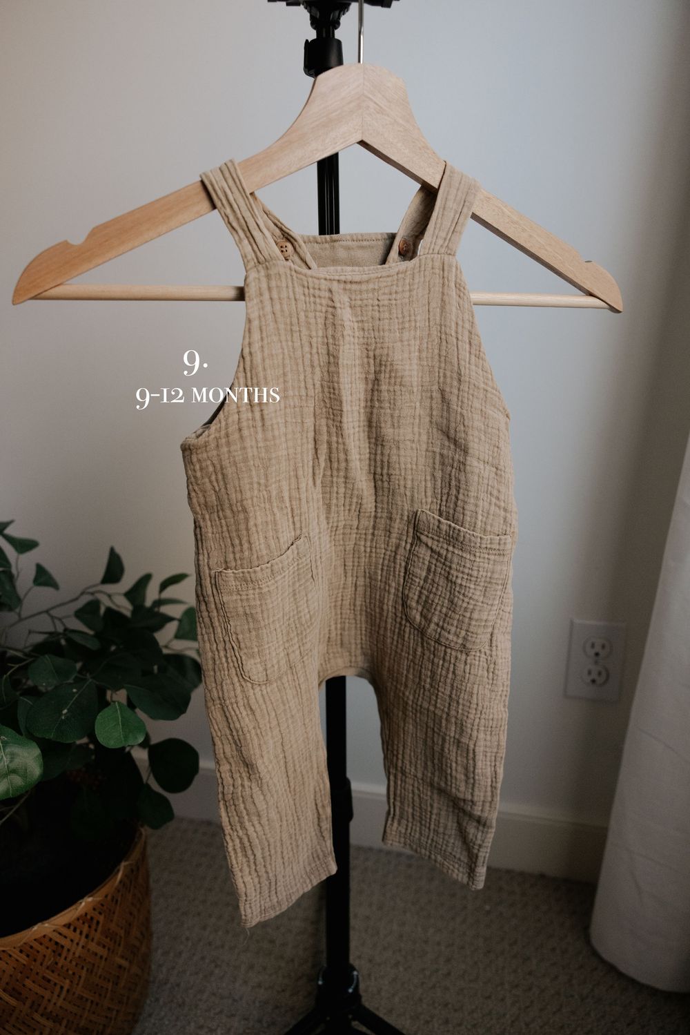 Neutral linen baby romper displayed on black stand with wooden hanger.