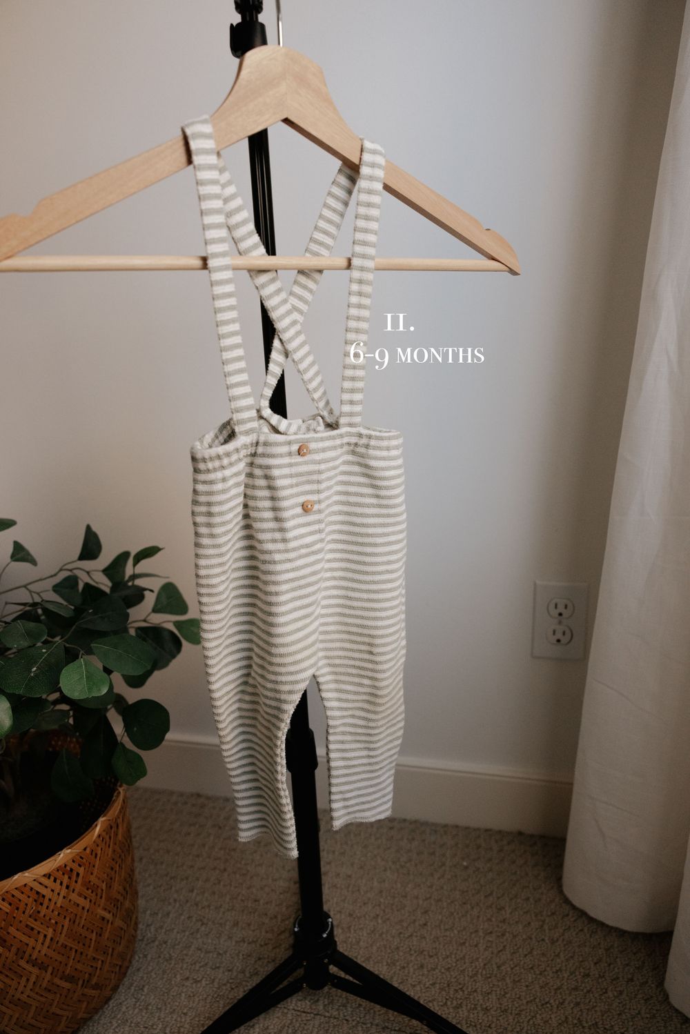 Gray and white striped baby onesie displayed on wooden hanger next to decorative basket.