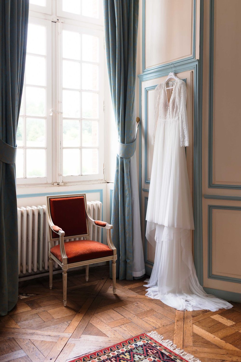 Elegant room with teal curtains, white dress, and herringbone wood floors.