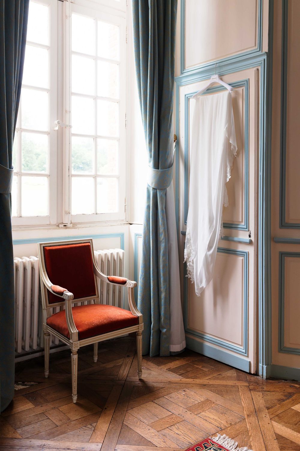 Elegant room with teal trim, red velvet chair, and white curtains.