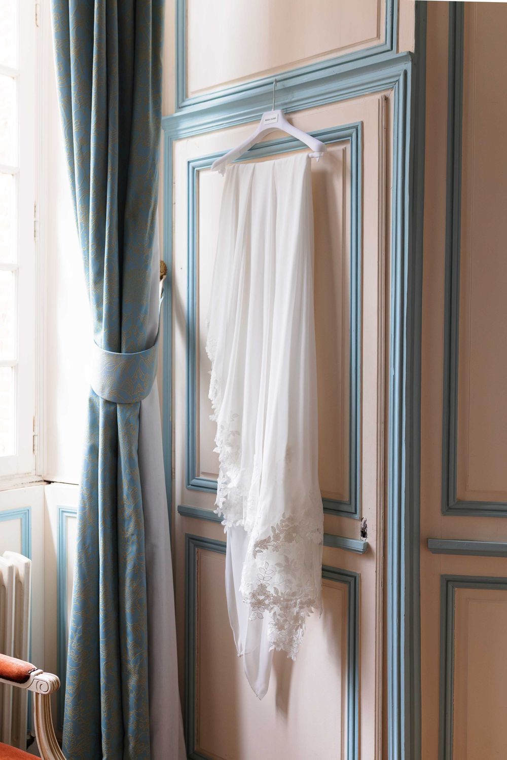 A white lace wedding dress hangs elegantly against blue-trimmed walls in a bridal suite.