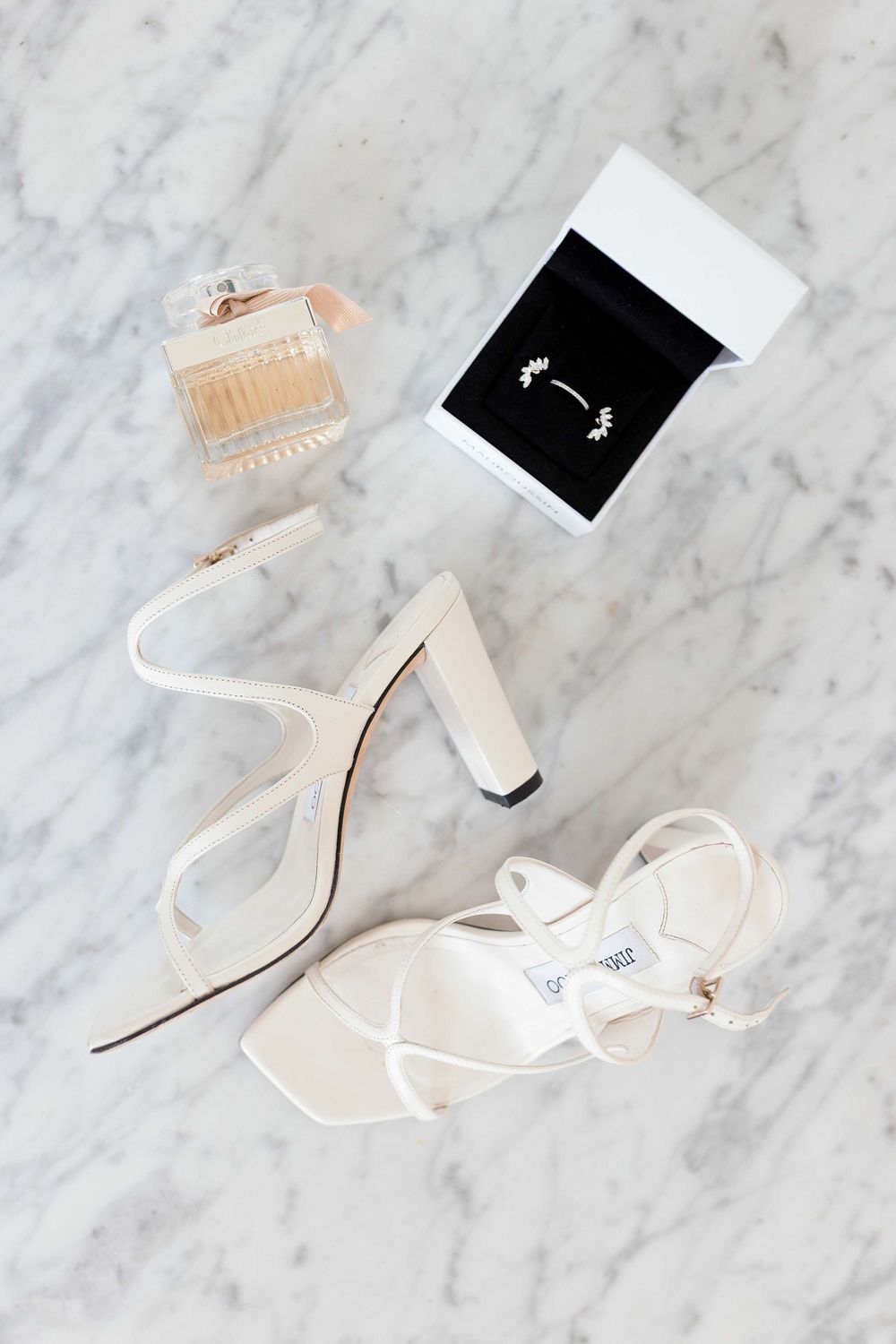 Elegant white strappy high heel sandals displayed on marble surface.