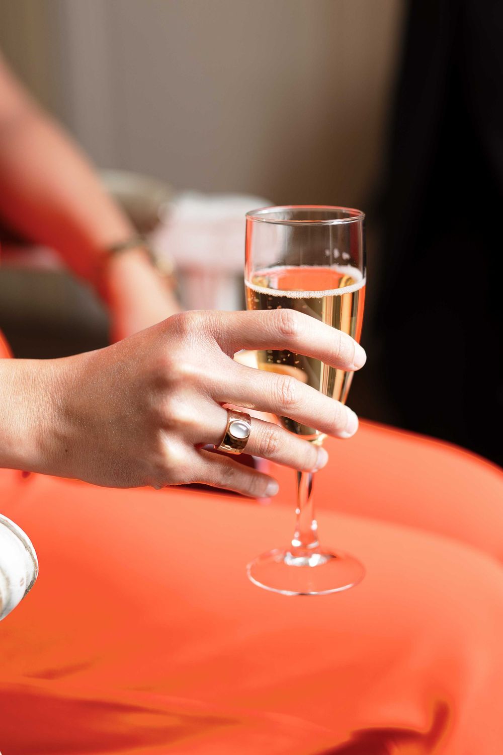 Hand holding champagne glass against coral-colored surface.