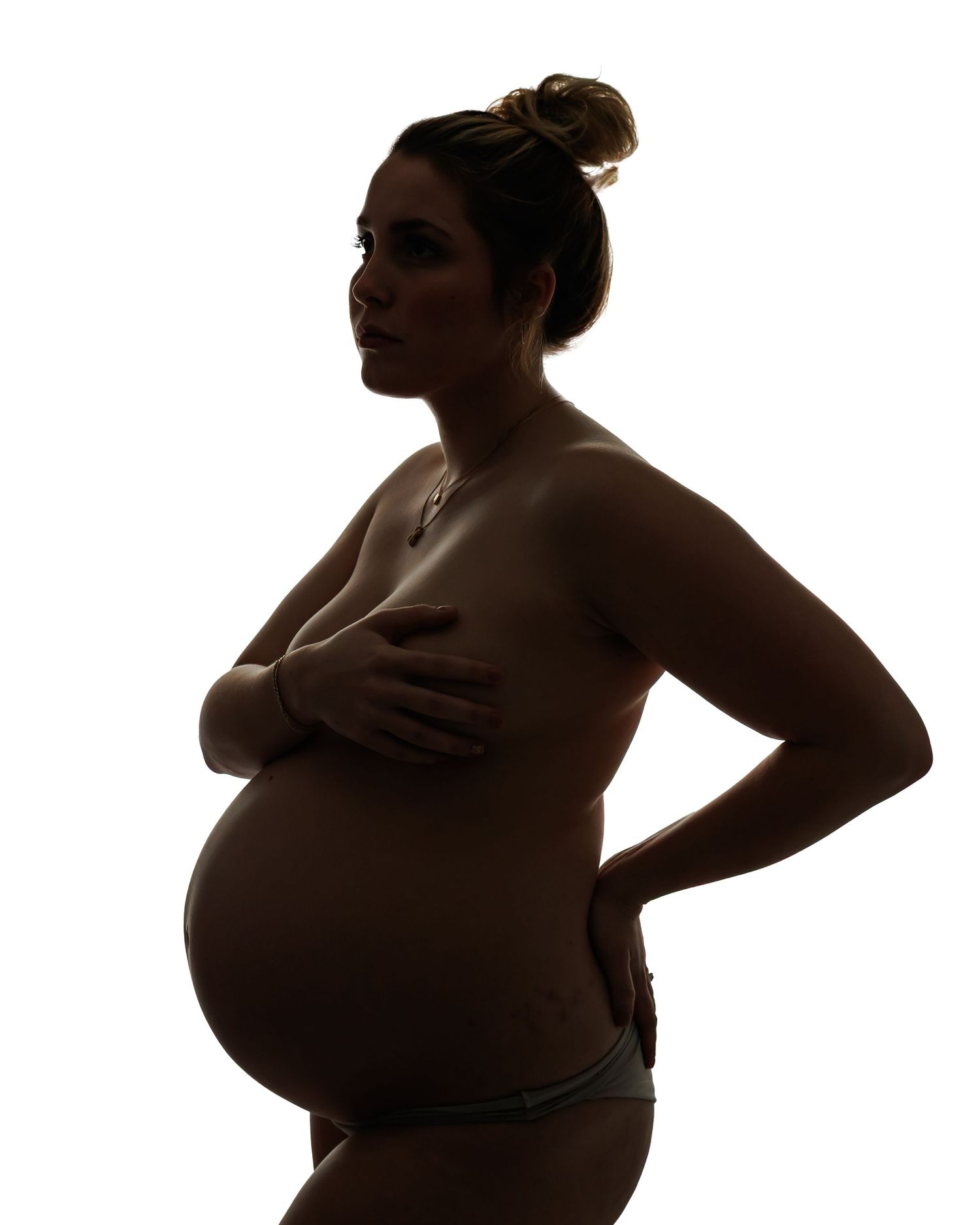 Dramatic maternity silhouette photograph of a pregnant woman in studio lighting, creating a timeless and artistic maternity portrait.