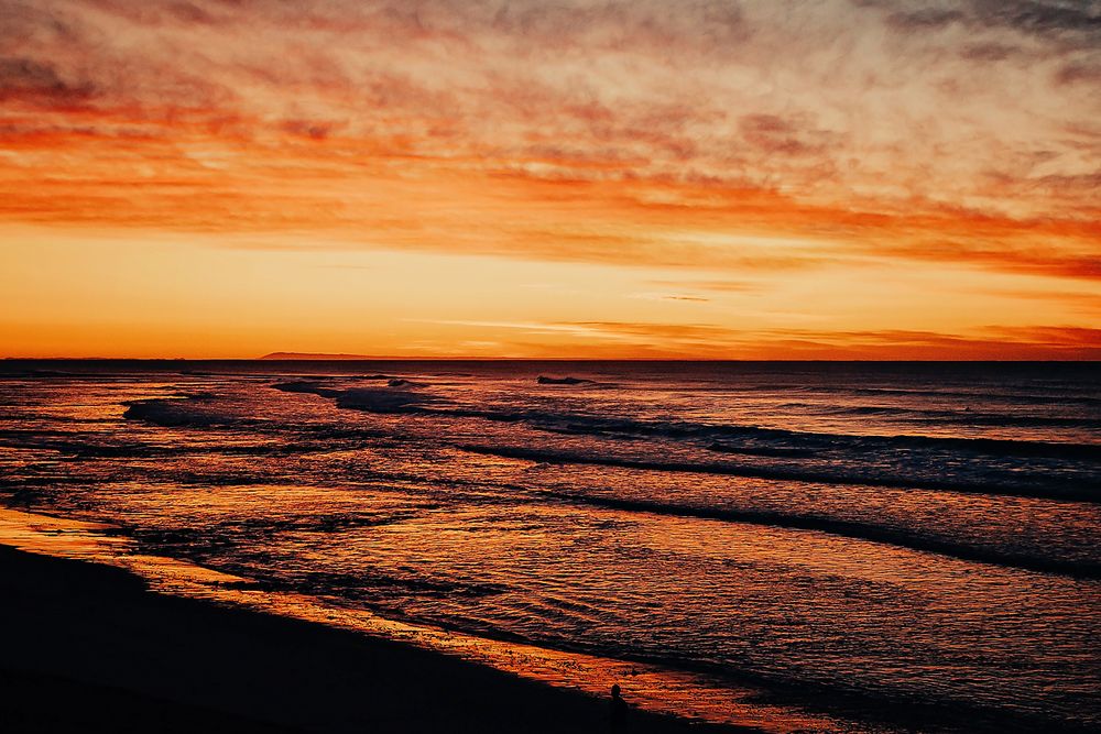 Dramatic orange and red sunset sky reflects on dark rolling ocean waves at twilight.