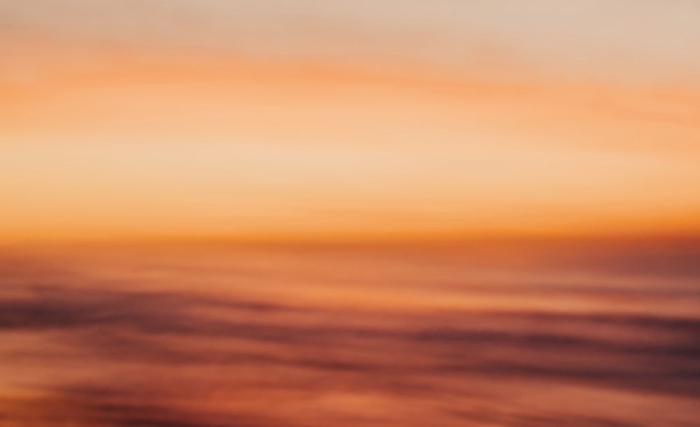 Vibrant orange and pink sunset sky with wispy clouds creates a dramatic panoramic view over the horizon.