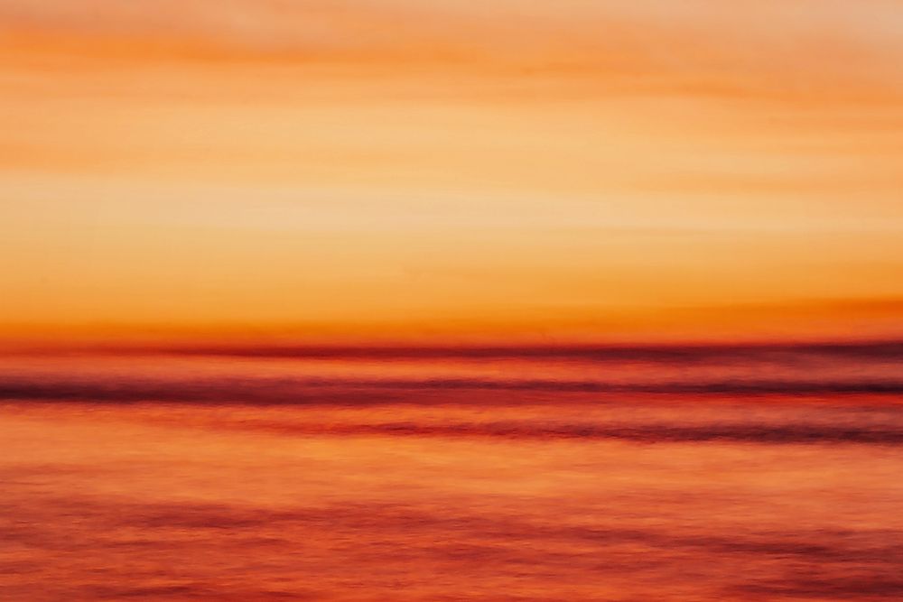 A stunning orange and red sunset creates a vibrant gradient across a tranquil ocean horizon.