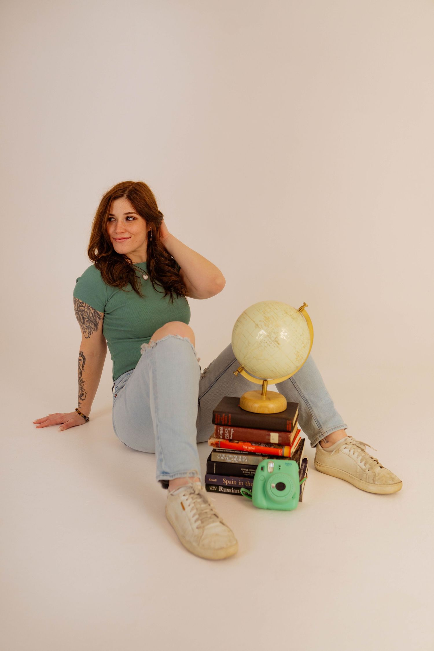 A person in a green shirt and jeans poses with vintage books, a globe, and a typewriter against a neutral background.