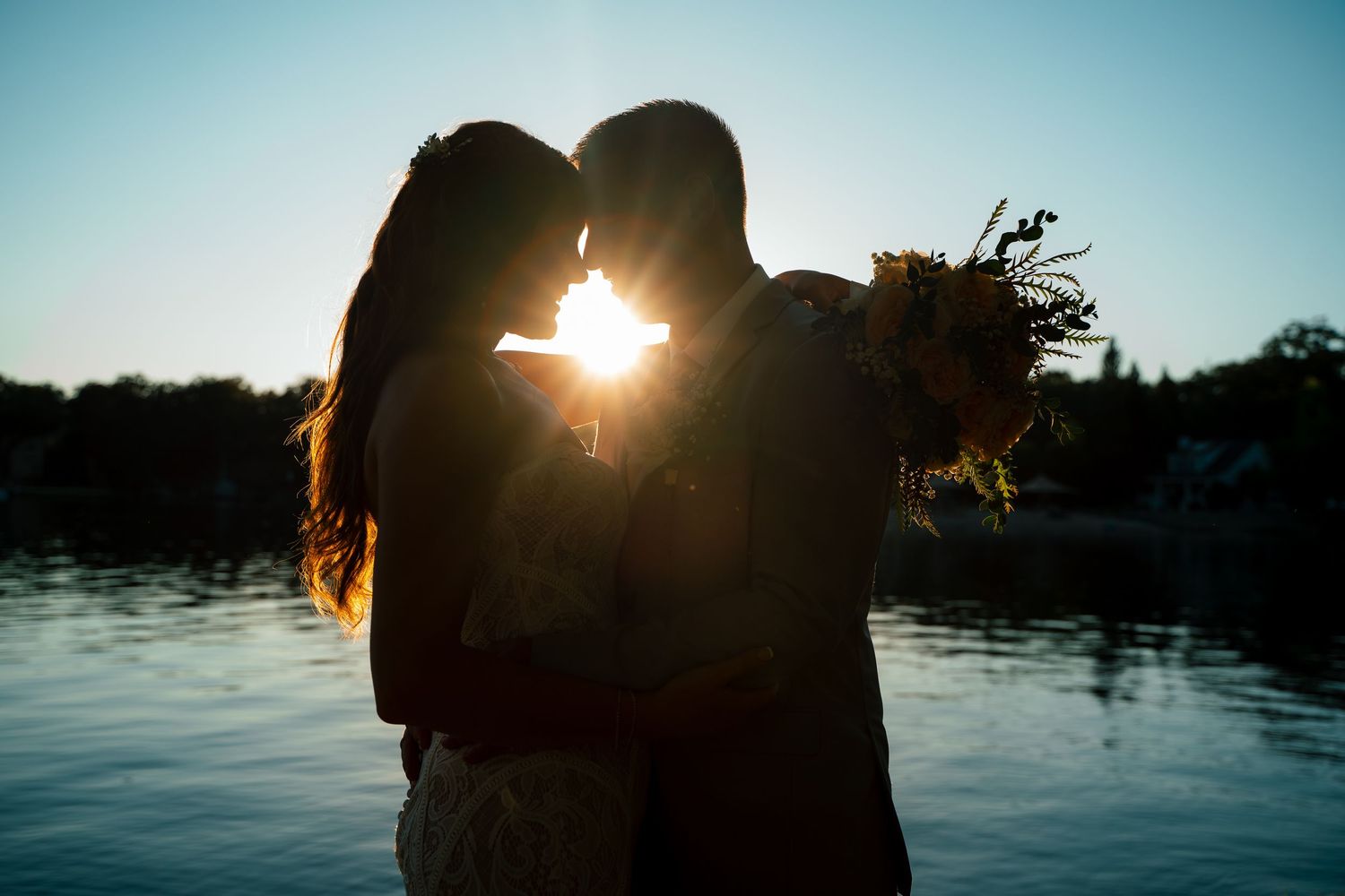 Silhouetted couple embraces against a glowing sunset over tranquil lake waters.