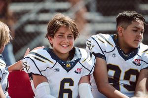 Saddleback Valley pop warner player number 6 sitting on the bench at halftime smiling at the camera.