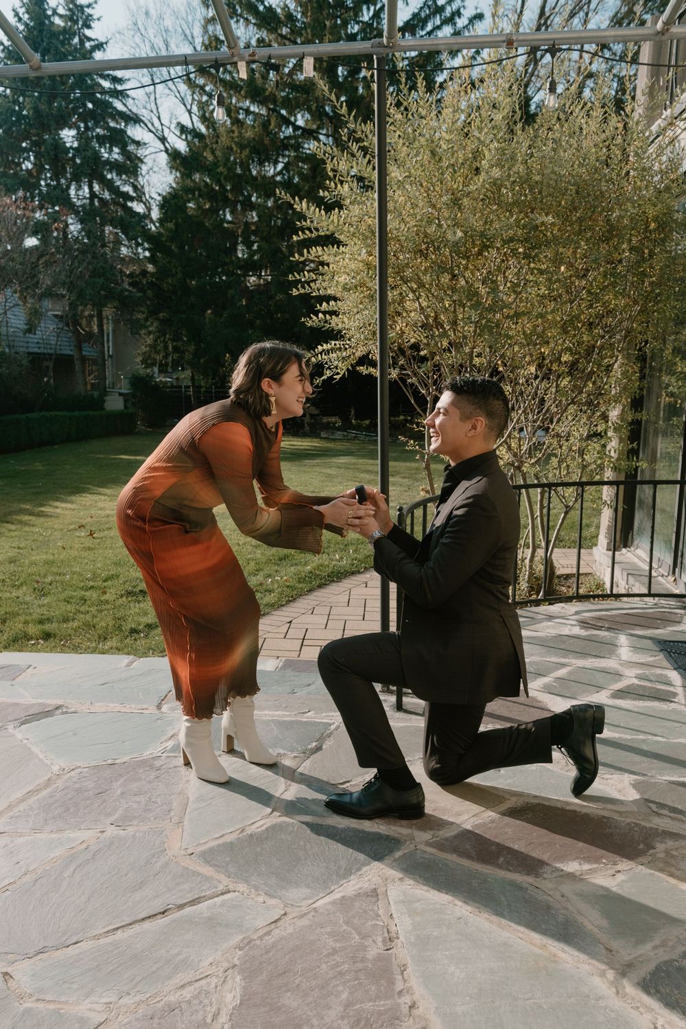 Two people in contrasting outfits perform a dynamic dance sequence on a sunlit porch with trees in the background.