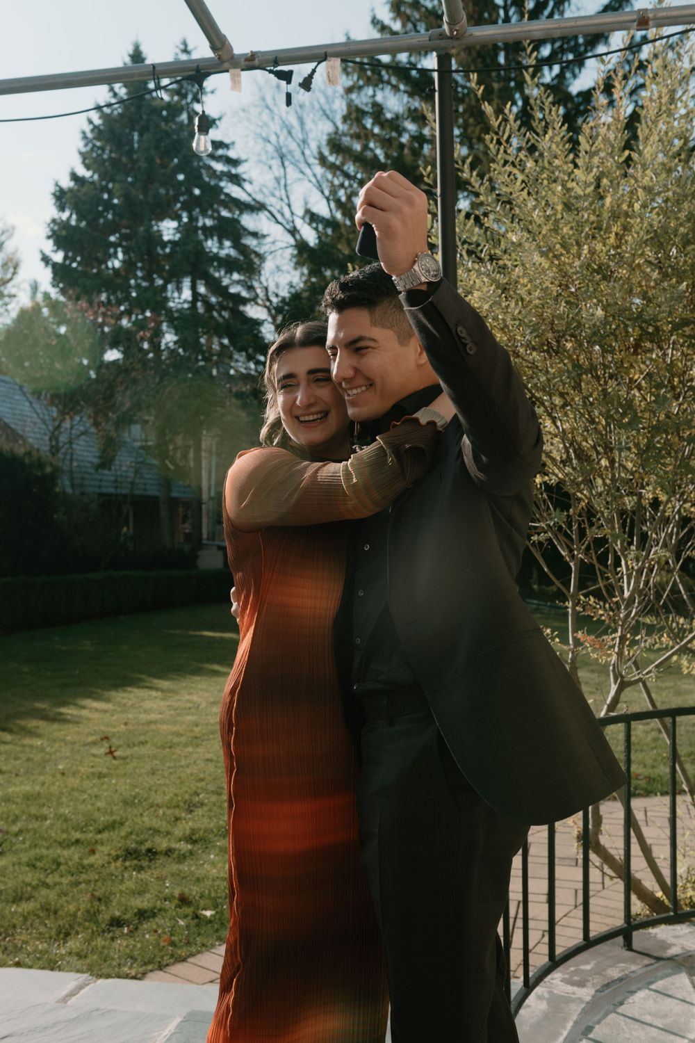 Two people share a joyful moment together while standing on an outdoor deck with trees in the background.