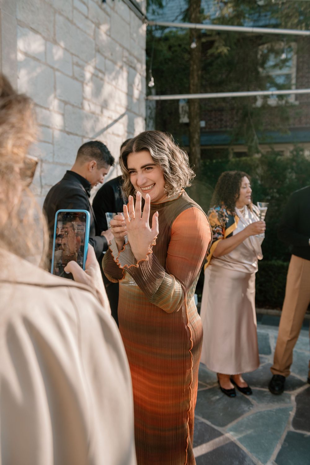 A group of people dancing and laughing together at an indoor social gathering with natural light streaming through windows.