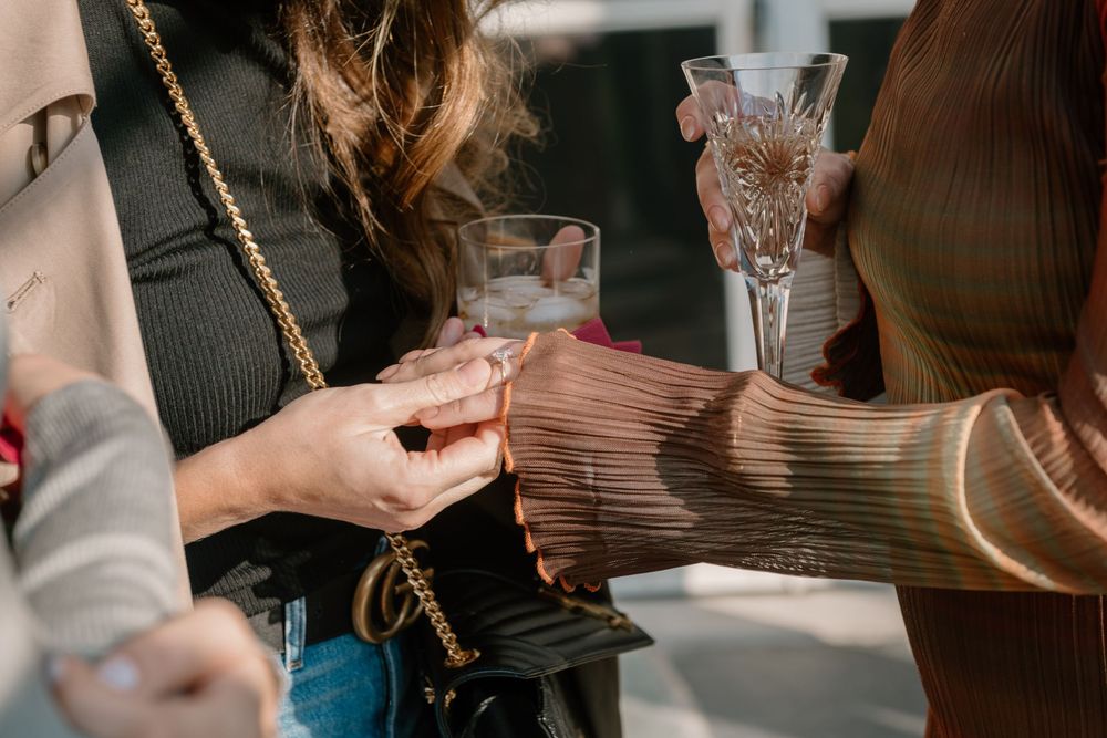 Person pouring a dark liquid from a glass bottle into a cocktail shaker at a bar counter.