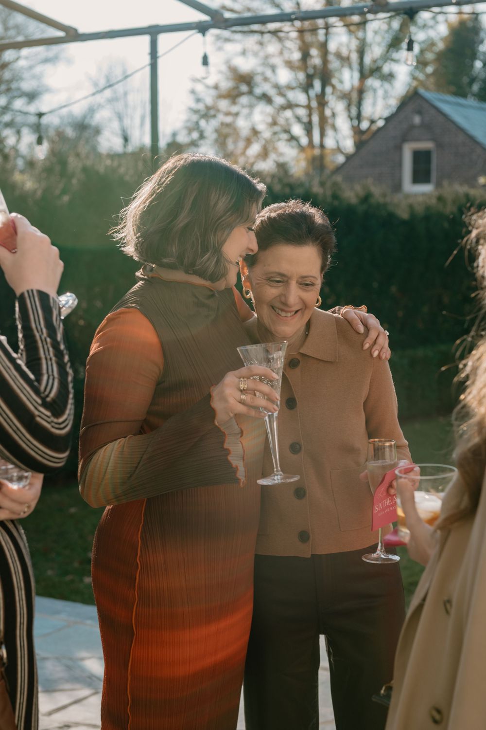 A group of friends in winter coats share laughter and drinks during an outdoor gathering.