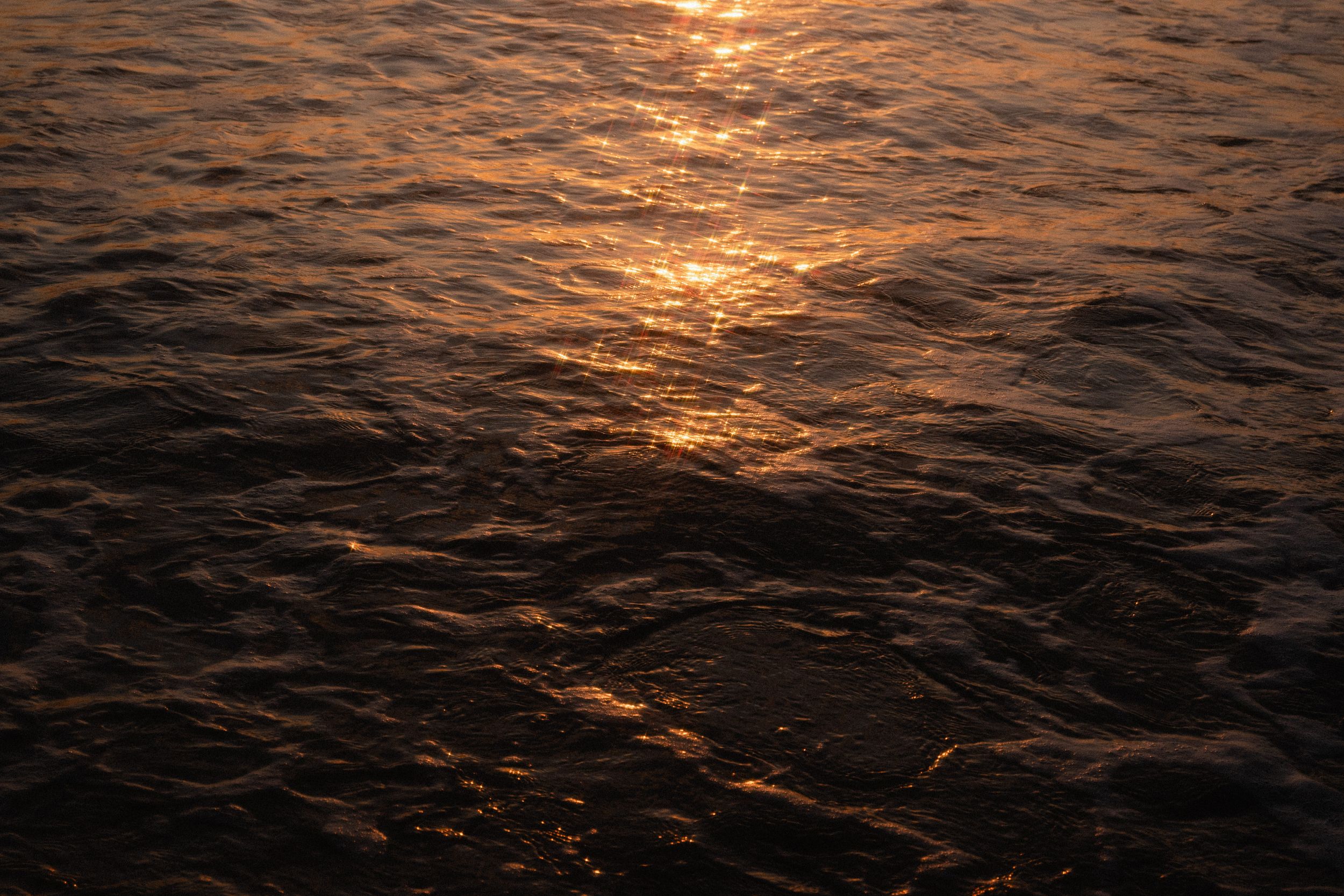 Dramatic golden sunset reflects on dark rippling ocean waves creating a mesmerizing pattern on the water's surface.