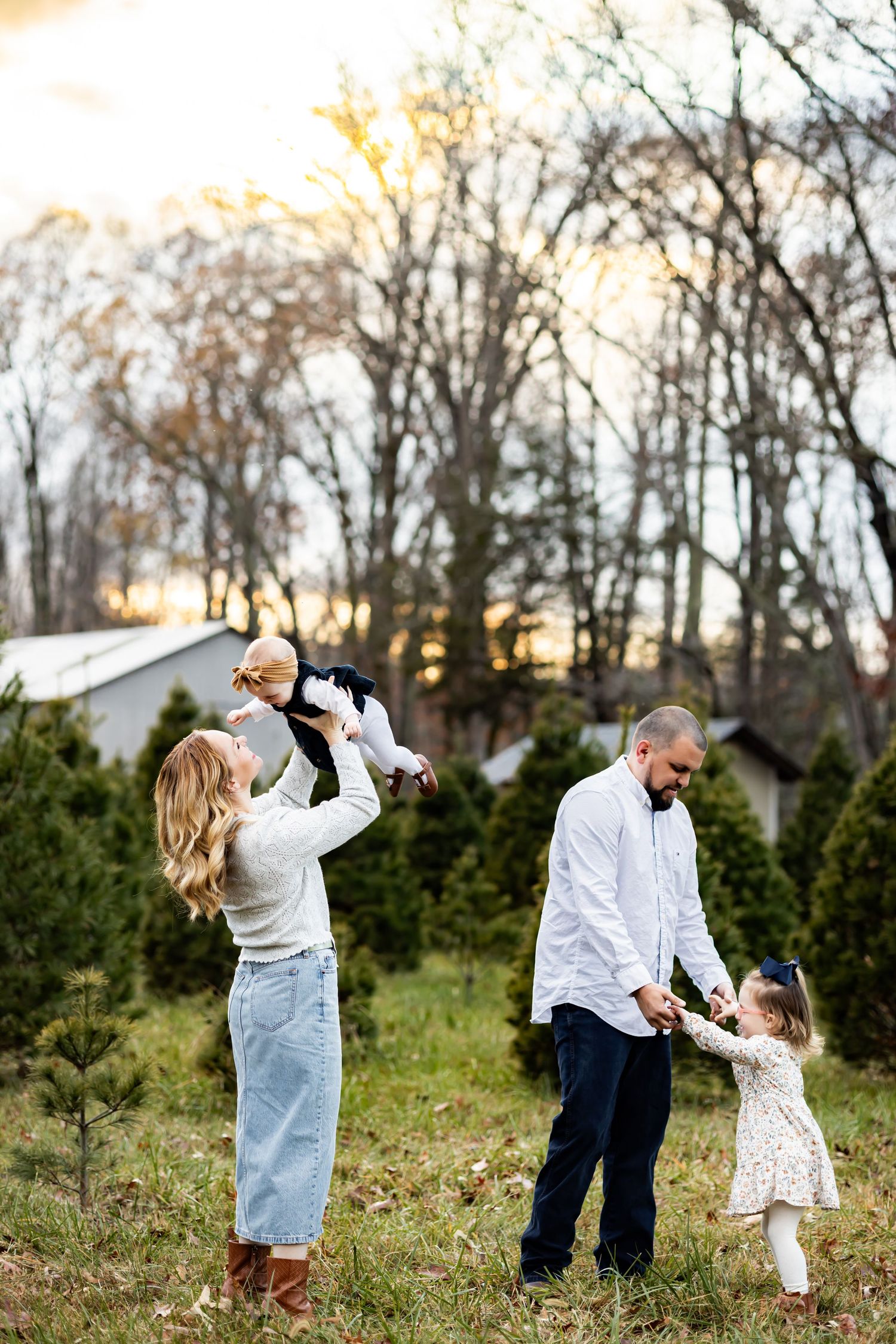 Family enjoying a playful moment together outdoors among evergreen trees at sunset. Family photographer in Richmond, Virginia. RVA photo