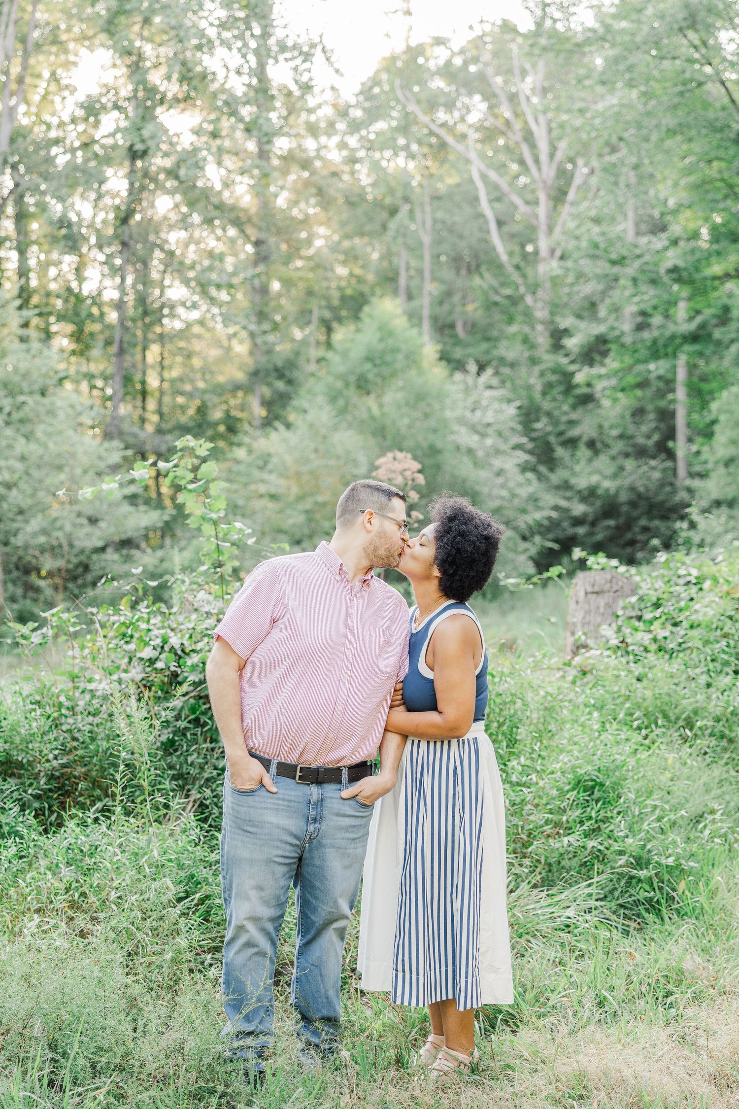 Couple sharing tender moment while walking through green woodland path.