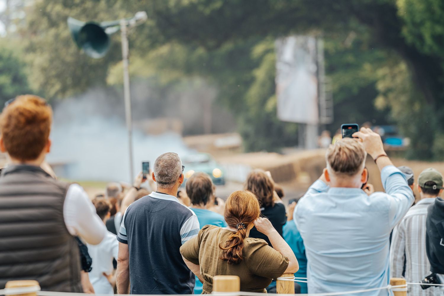 Crowd of spectators watching an automotive event from behind barriers.