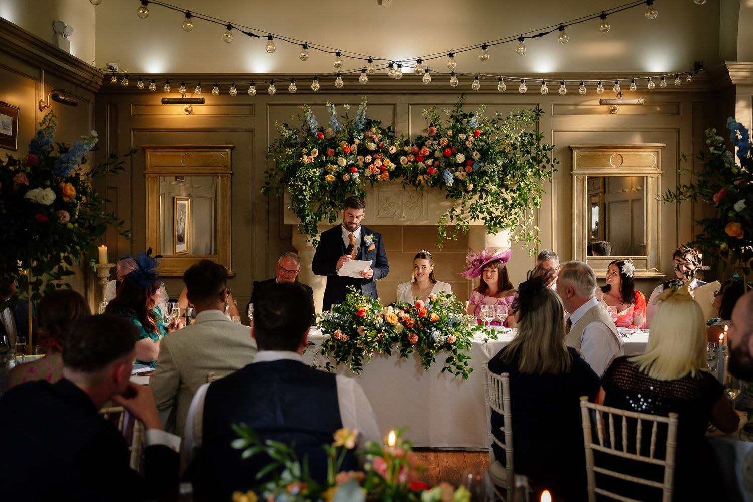 Evening wedding reception with ambient lighting and decorated tables filled with guests. Ellingham Hall
