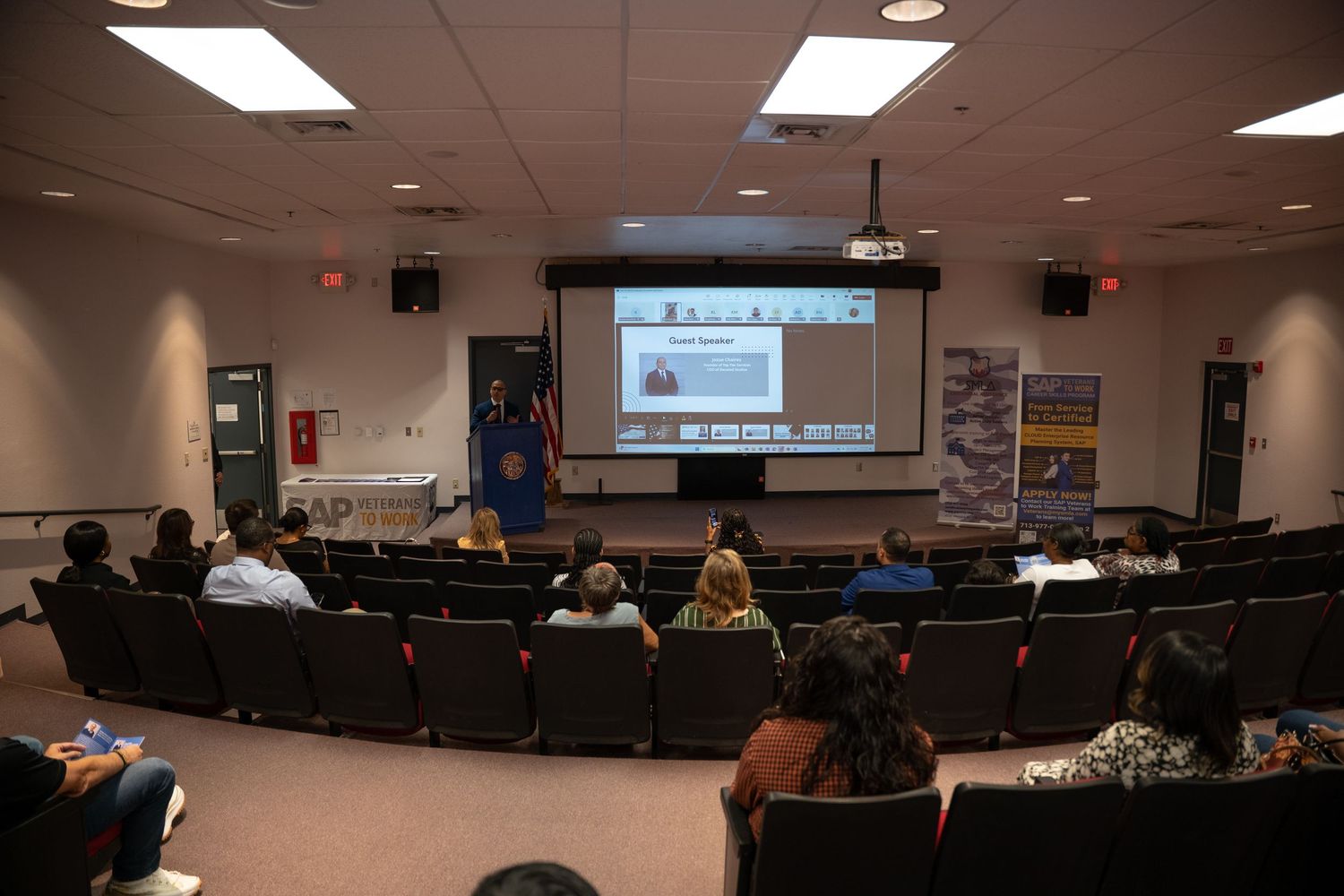A dimly lit conference room with fluorescent lighting and rows of tables and chairs arranged in a classroom style setup.