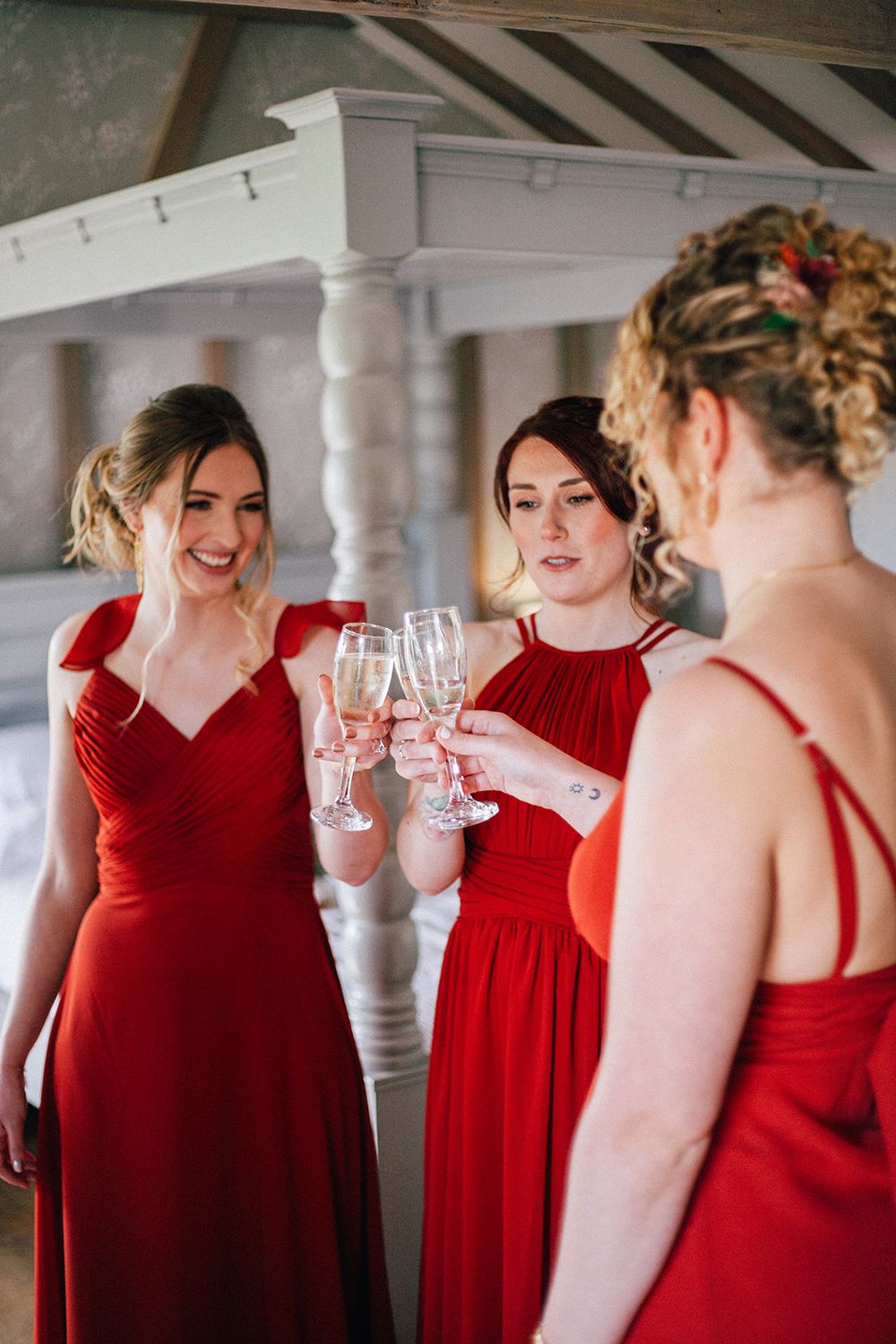 Bridesmaids in flowing red dresses gather for celebratory champagne toasts at an elegant indoor venue.