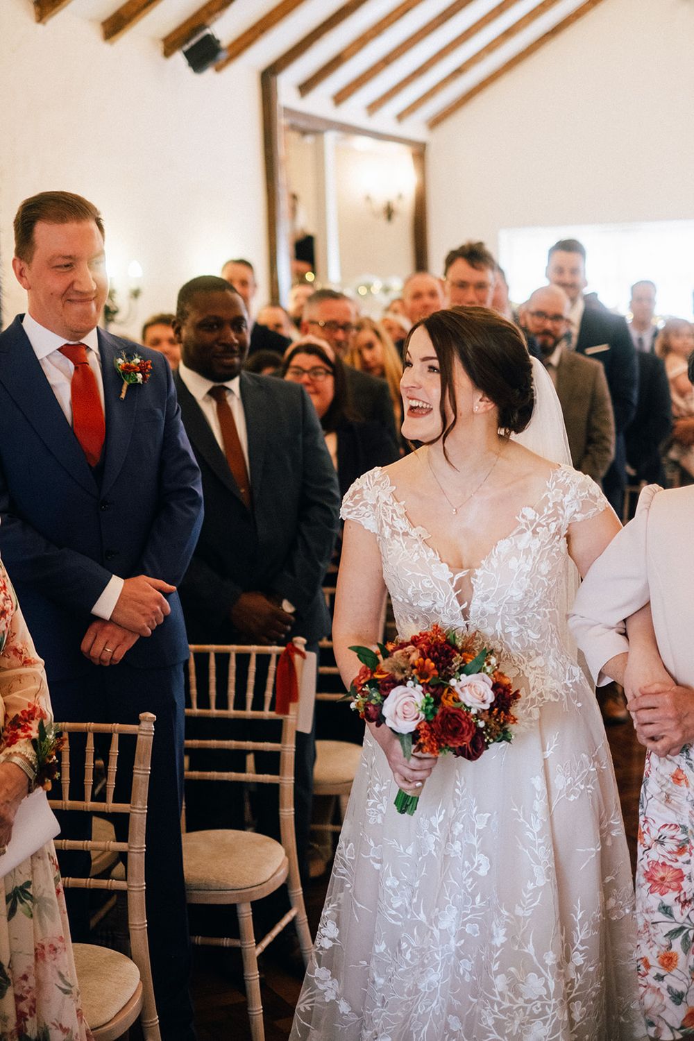 Wedding ceremony guests stand in rows of chairs while a bride in a white lace dress walks down the aisle.