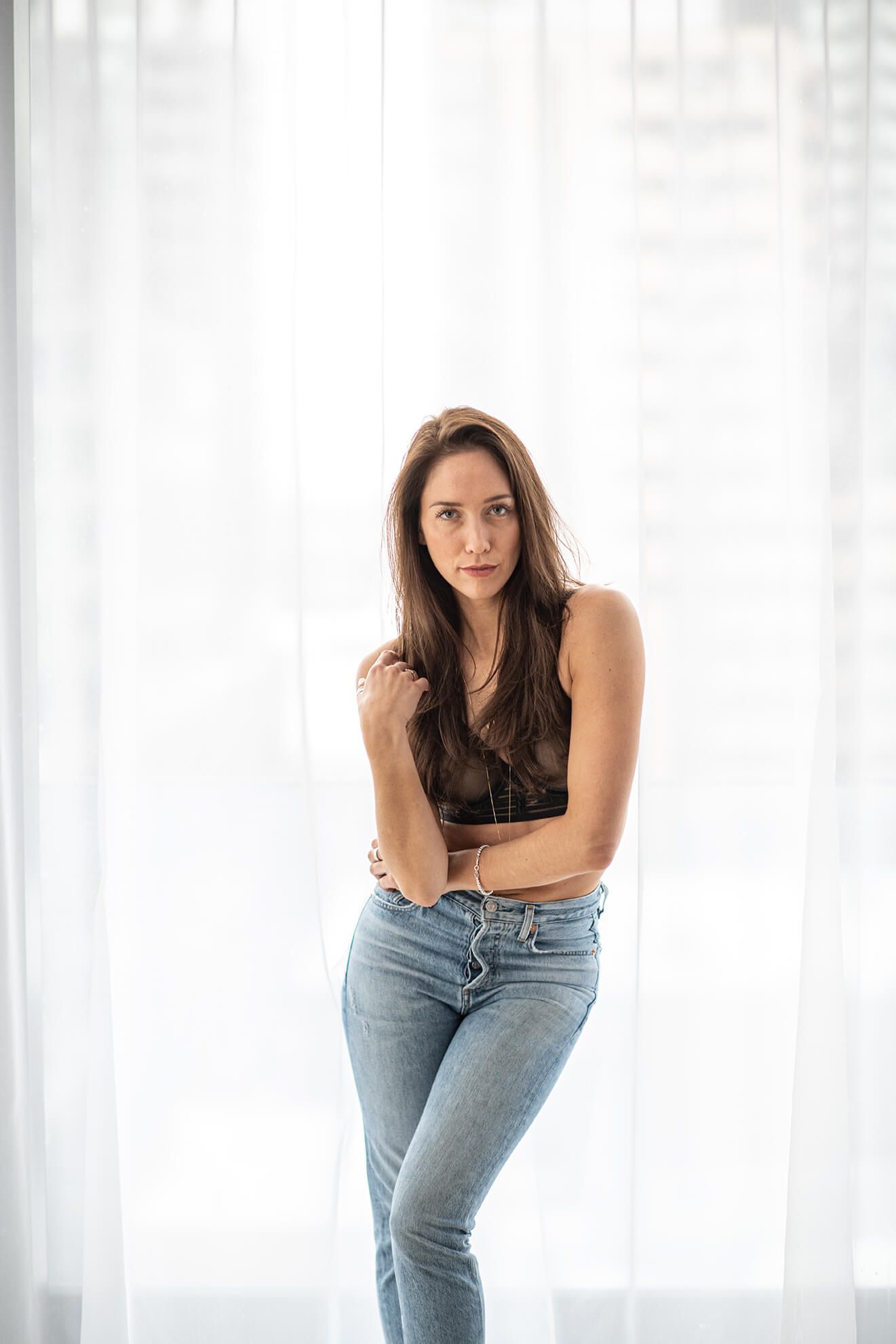 Fashion model poses in casual denim and black top against white backdrop in artistic portrait series.