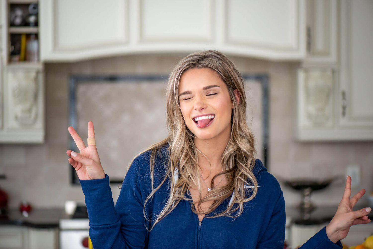 Lifestyle portrait of woman in navy shirt showing peace sign in modern kitchen.