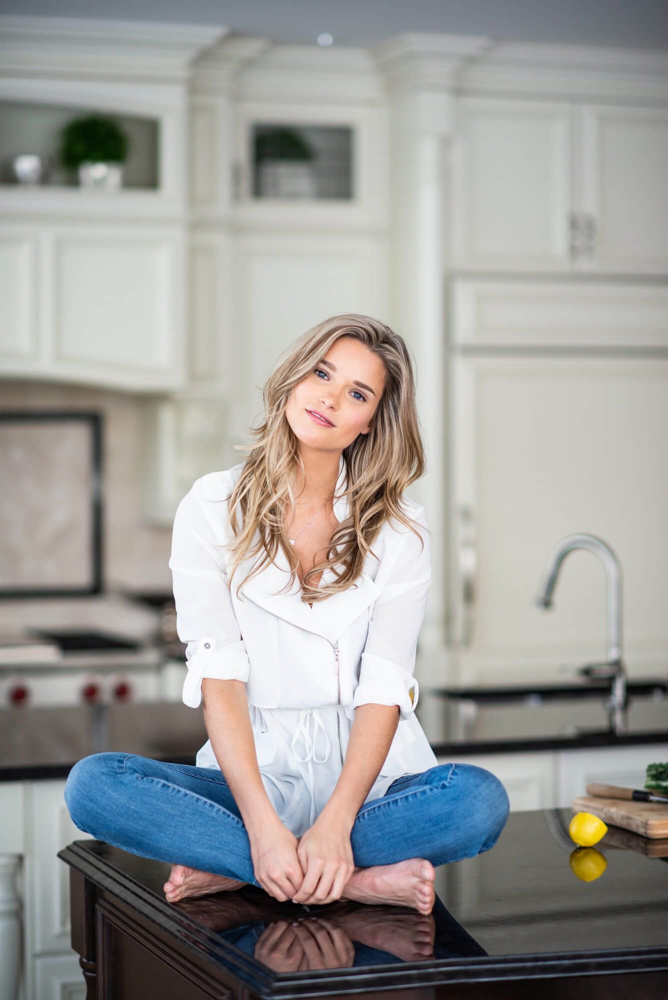 Casual lifestyle portrait of woman in white shirt and jeans sitting on kitchen counter.