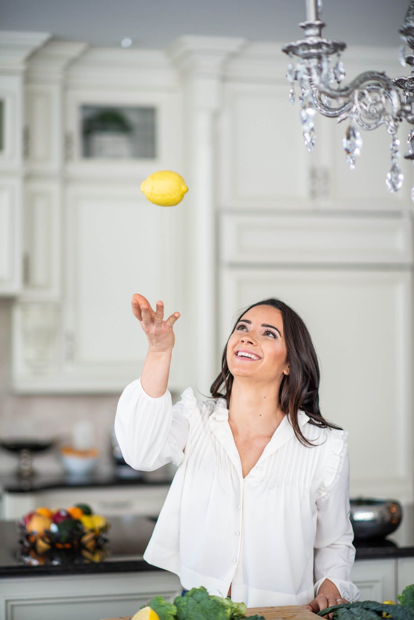Joyful moment juggling lemon in elegant kitchen with chandelier.