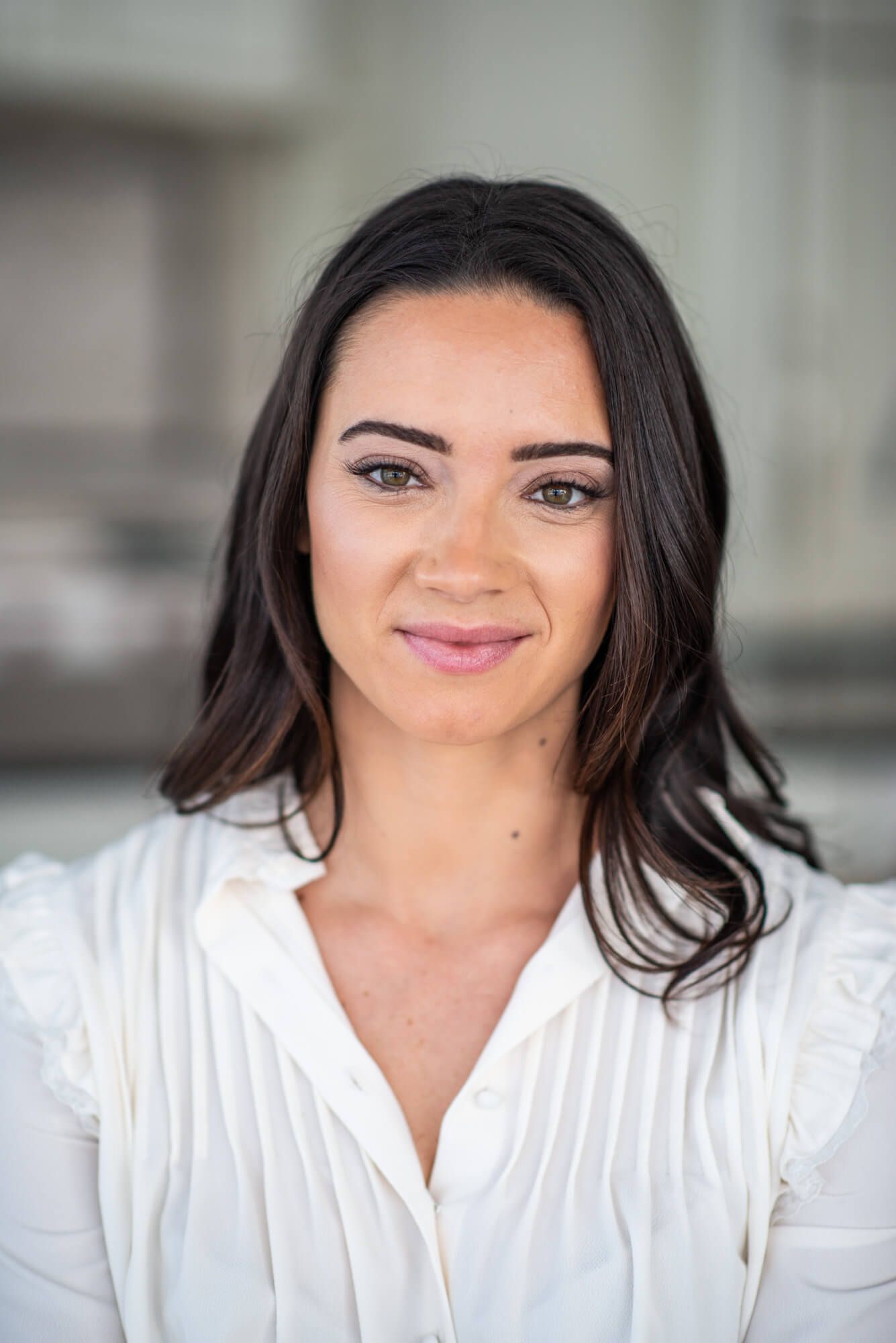 Portrait in white pleated blouse against neutral background.